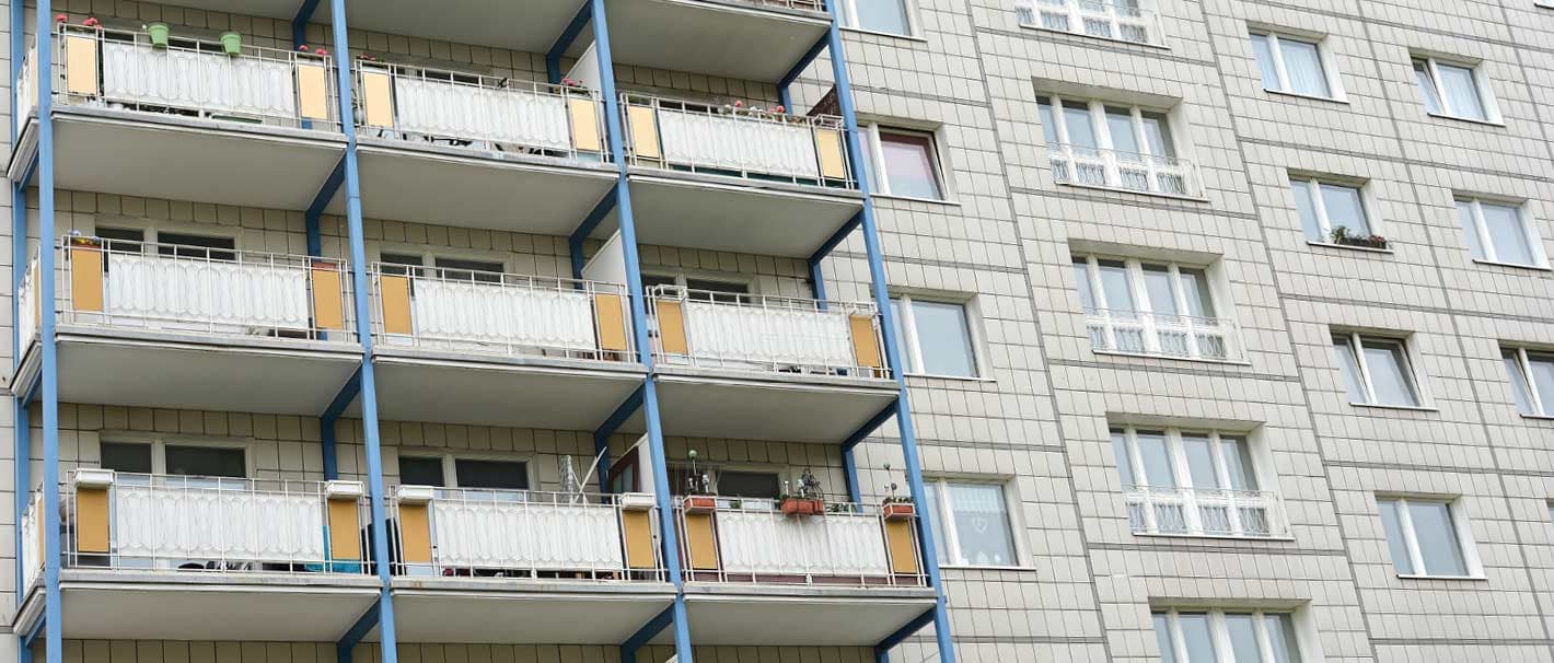 Trostlose Fassade eines Wohngebäudes. Die eine Hälfte der Wohnungen hat einen Balkon, die andere nicht.