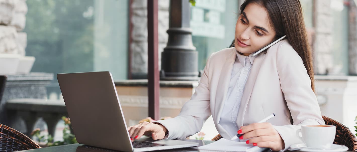 Junge Frau sitzt mit Laptop im Homeoffice und telefoniert.