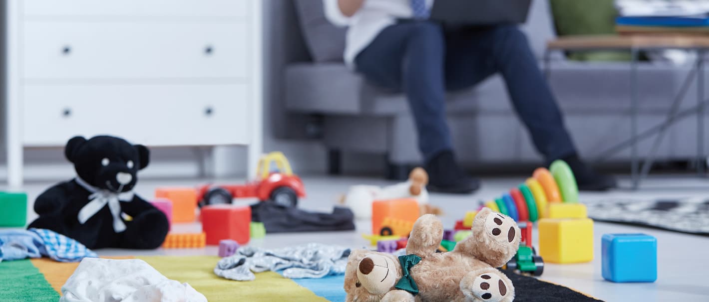 Mann sitzt mit Laptop auf der Couch, auf dem Boden liegt Kinderspielzeug