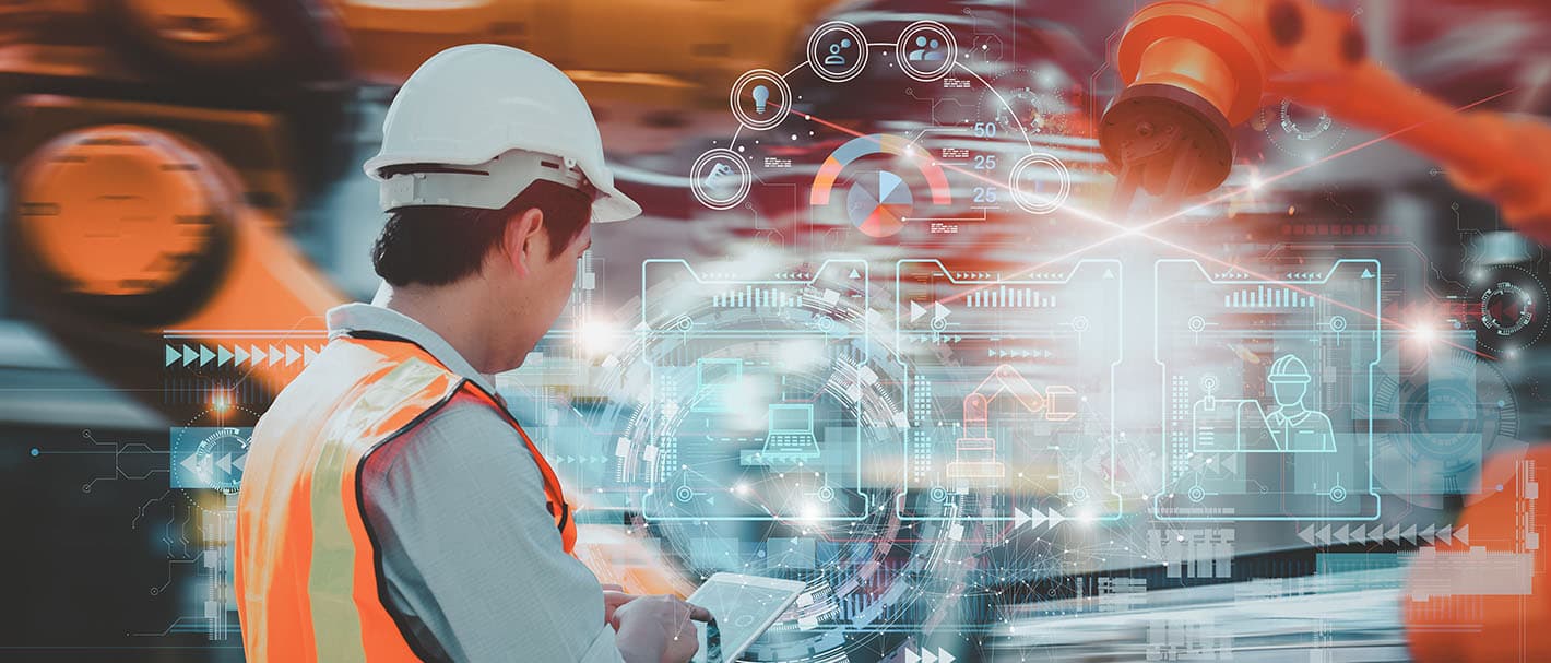 Industriearbeiter in mit Warnweste und Helm von hinten, der über ein Tablet Roboterarme steuert.