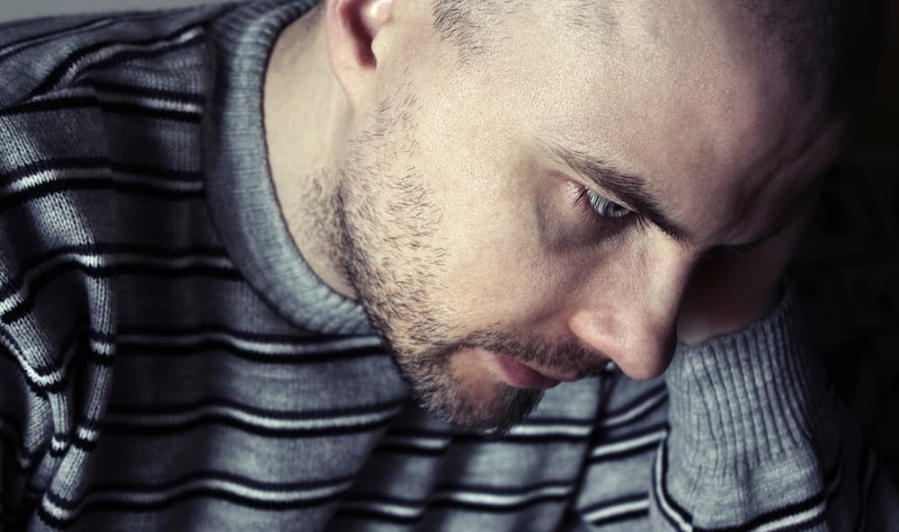 Mann mit psychischer Erkrankung stützt den Kopf auf die Hände.