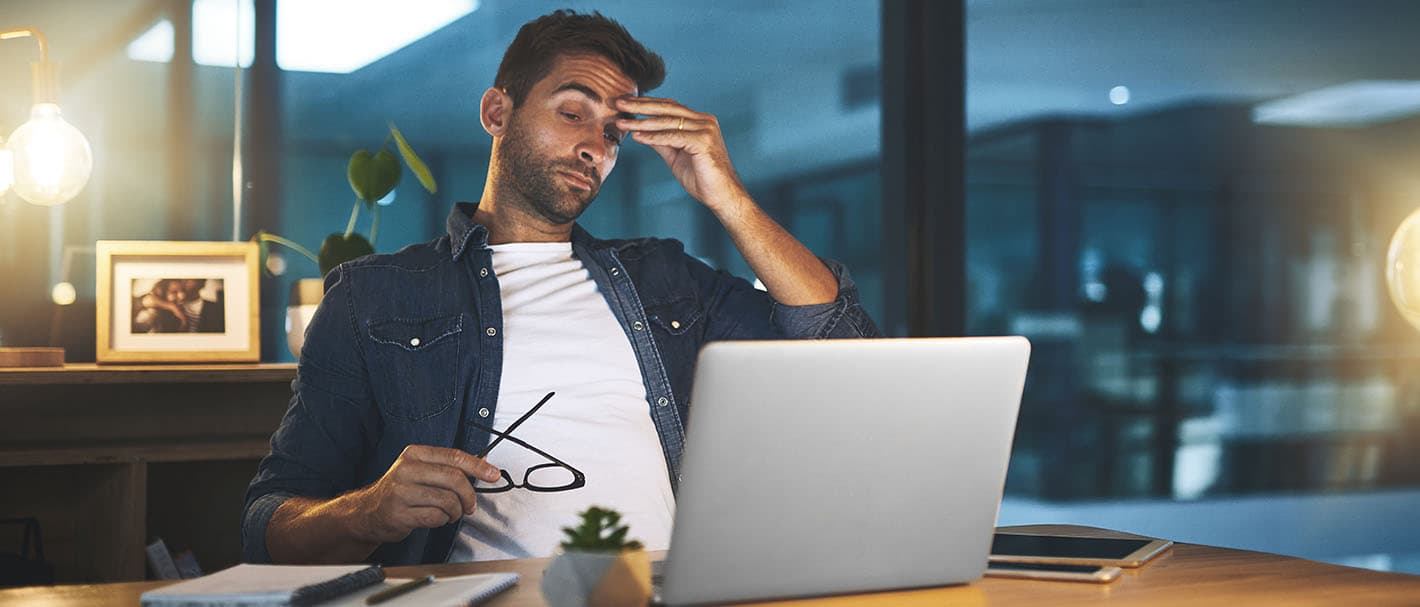 Ein Mann, der nachts im Büro arbeitet, reibt sich müde die Stirn