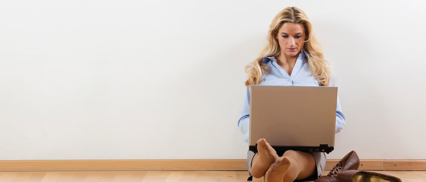Junge Frau sitzt mit Laptop auf dem Fußboden