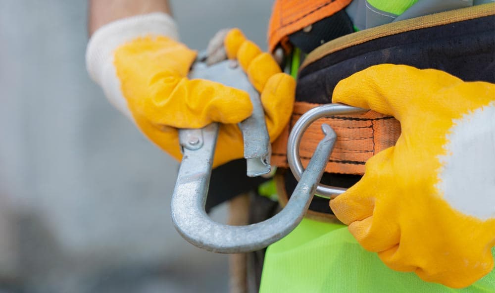 Eine Arbeitskraft sichert sich für ihren Einsatz mit einem Karabinerhaken.