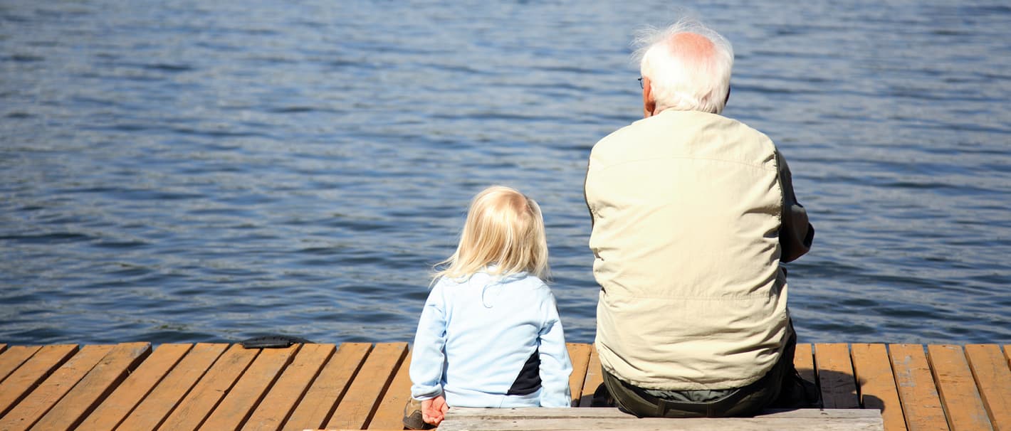 Opa und Enkelkind sitzen auf einem Steg und schauen aufs Wasser