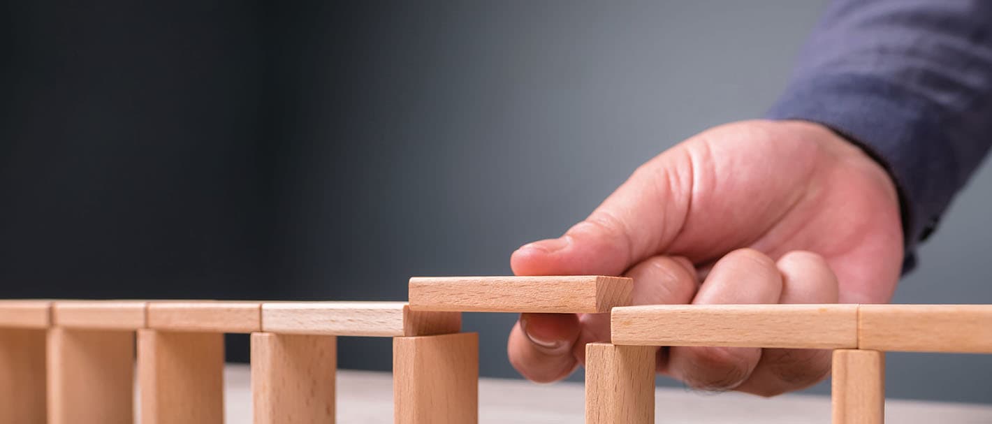 Eine Männerhand baut eine Holzbrücke aus Miniaturklötzchen.