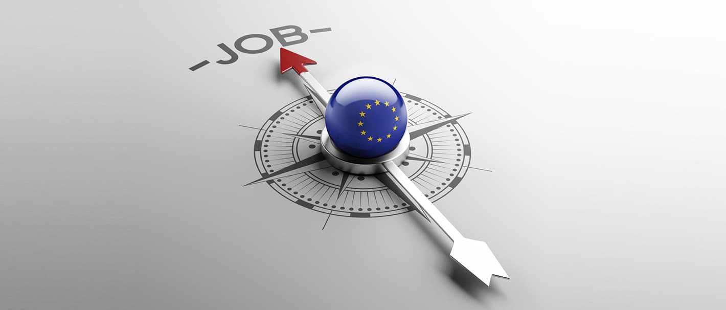 Kompass mit Murmel in der Mitte, auf der die EU-Flagge abgebildet ist. Die Kompassnadel zeigt auf das Wort "Job".