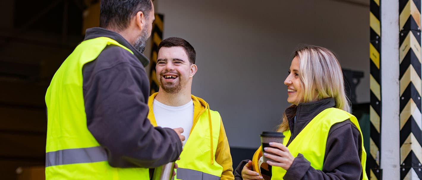 Ein Mann mit Down-Syndrom und seine Kollegen machen eine Arbeitspause und trinken Kaffee und heißen Tee draußen auf einer Laderampe.